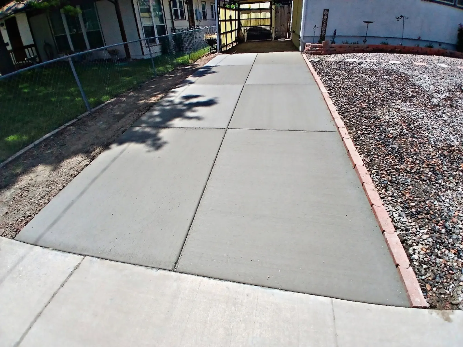 The finished driveway — a smooth jointed concrete drive running to a carport, edged with brick against gravel.