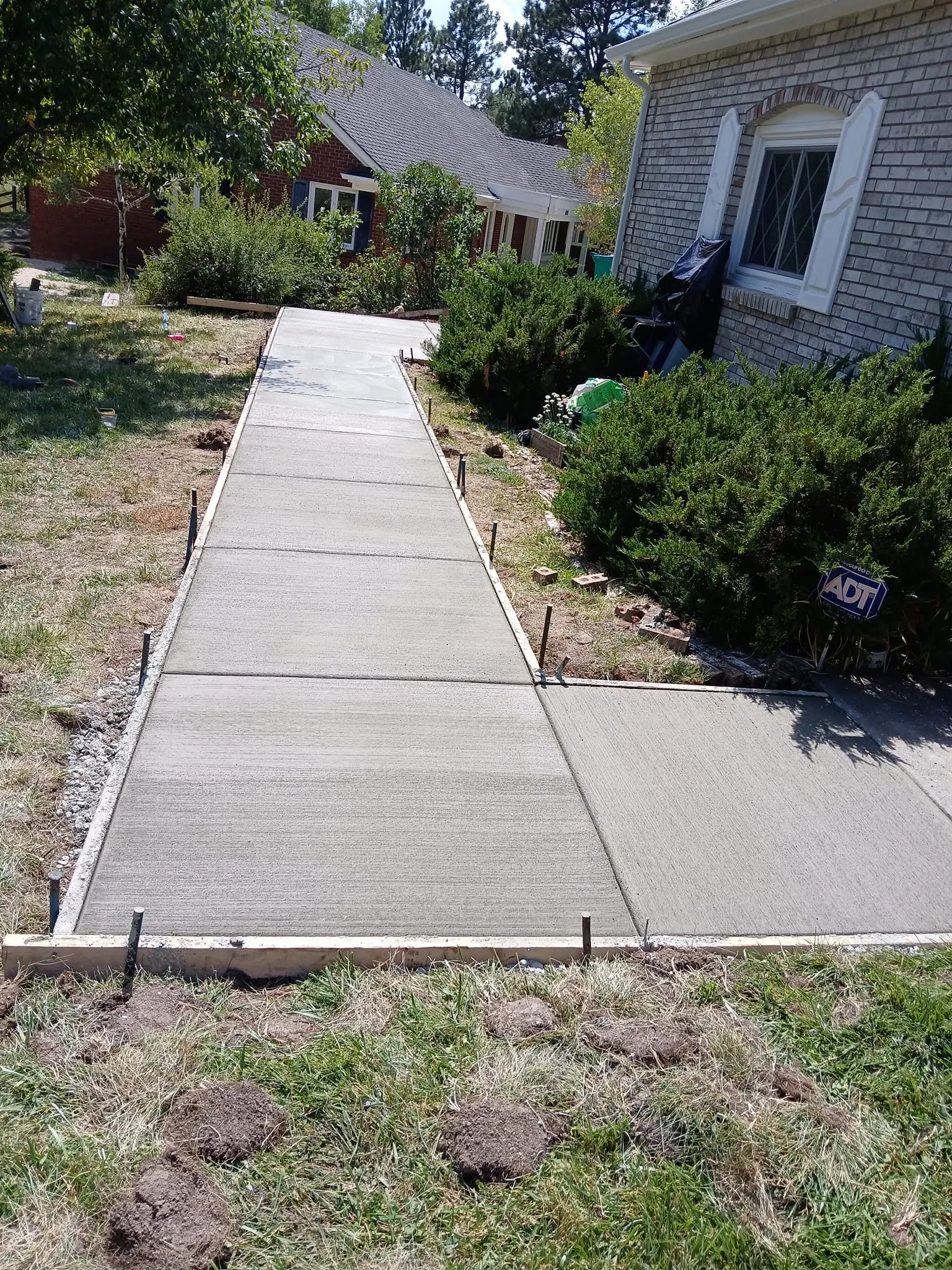 The same walkway finished — a broom-finished concrete path and landing running alongside a brick house.