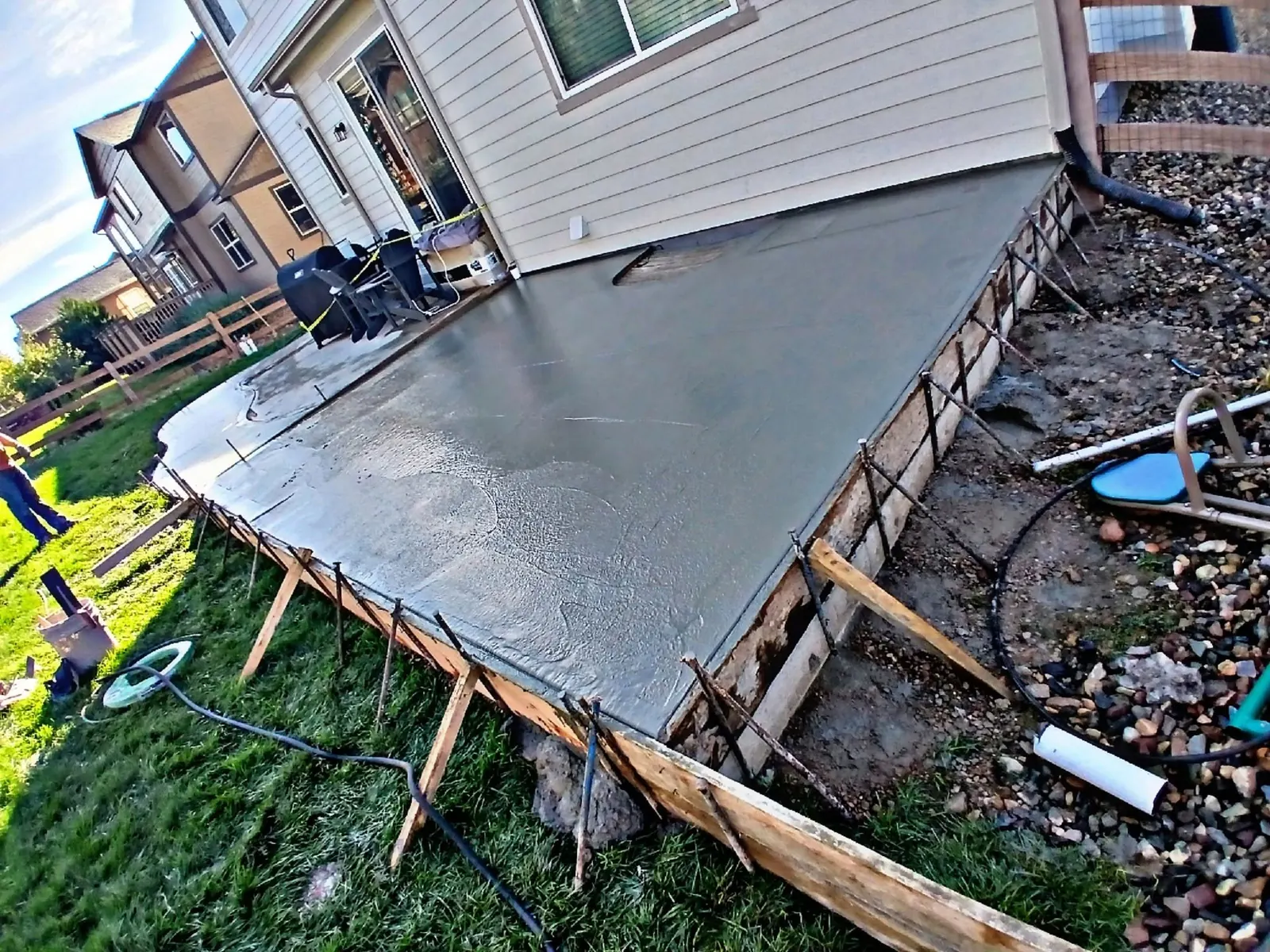 A freshly poured back patio, still wet and floated smooth, with timber forms and stakes around the edge.