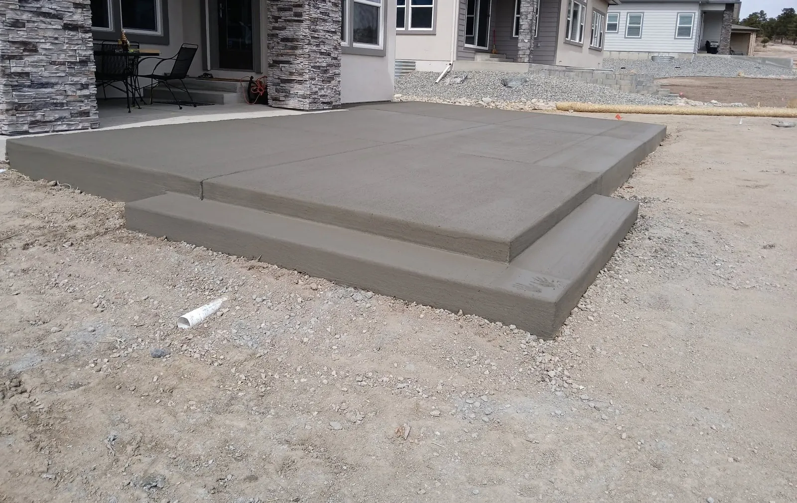 A raised broom-finished patio slab with a broad full-width step down to the yard, at a new stone-and-stucco home.