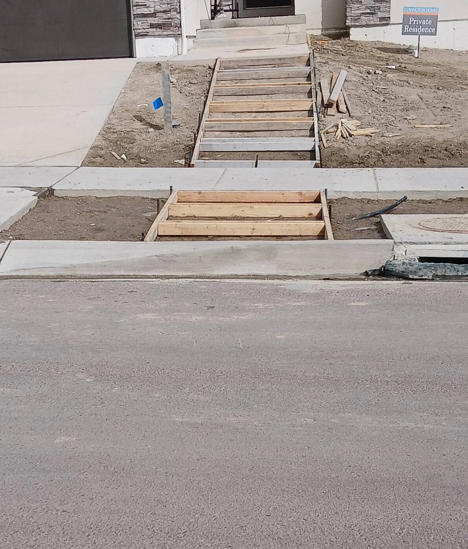 Timber forms for front entry steps and a landing at a new-build house, set between a finished sidewalk and bare dirt.