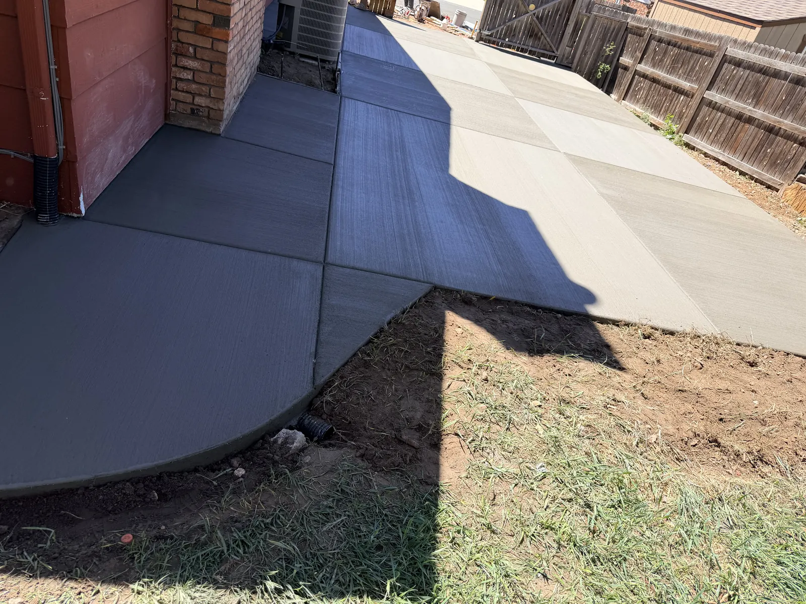 A broom-finished concrete slab along the side of a house, ending in a curve where it meets the lawn.