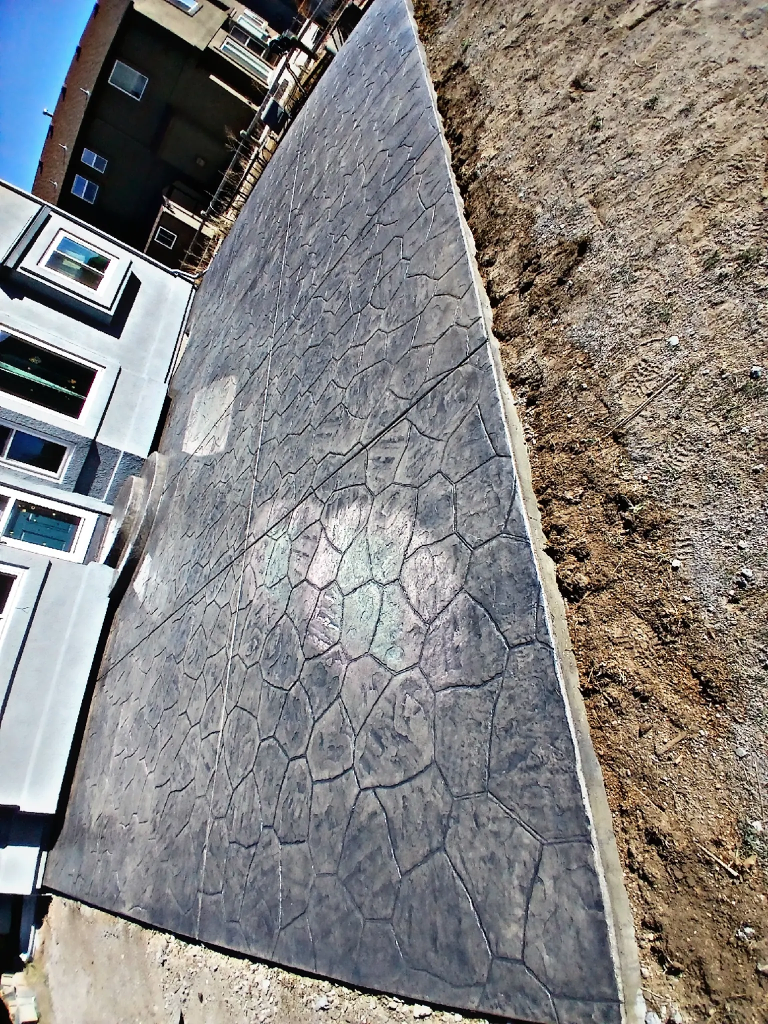 A narrow charcoal stamped concrete slab running along the side of a house, photographed looking up its length.