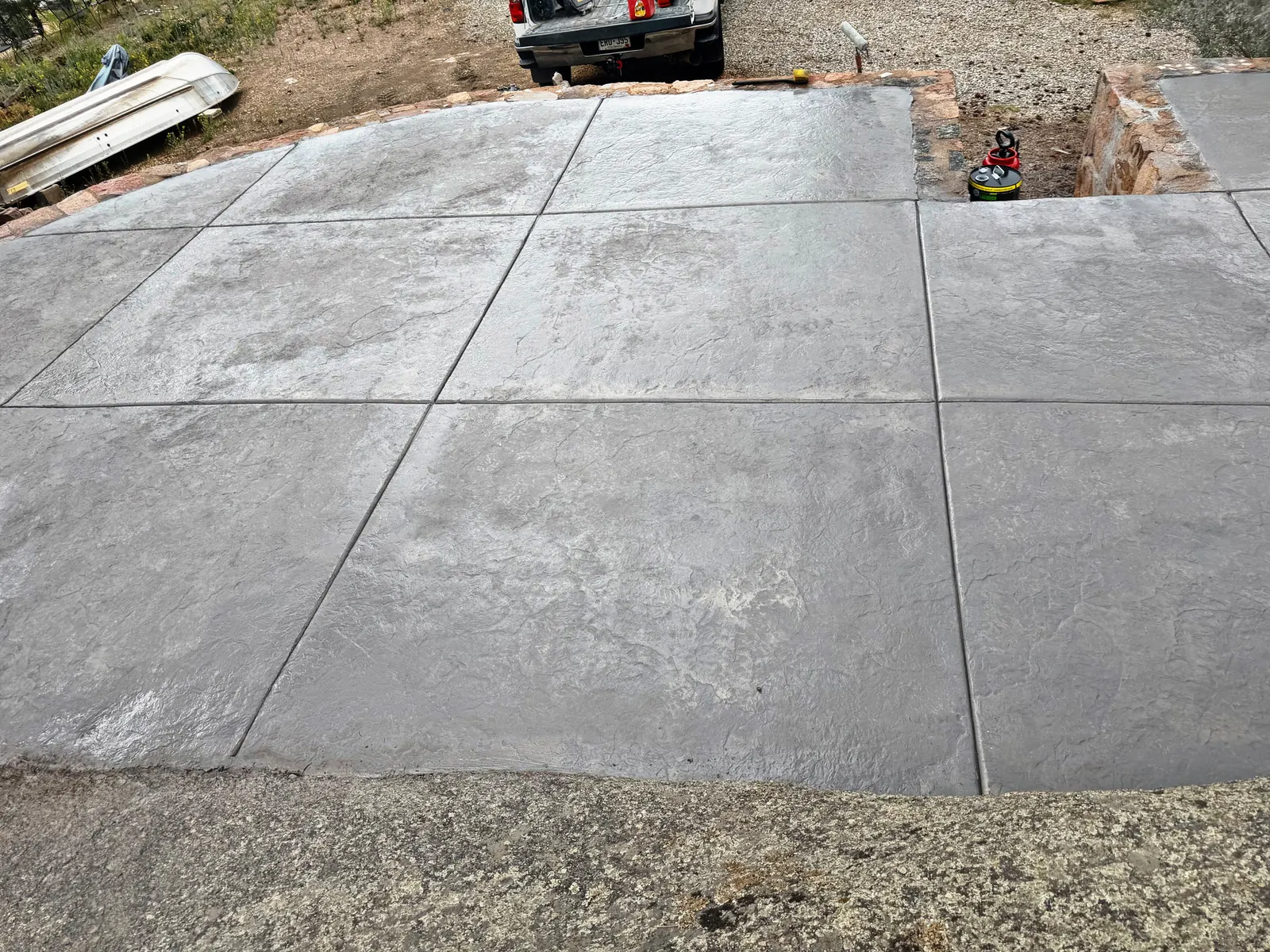 A grey texture-stamped concrete slab inside a low stone border, divided into large panels by control joints.